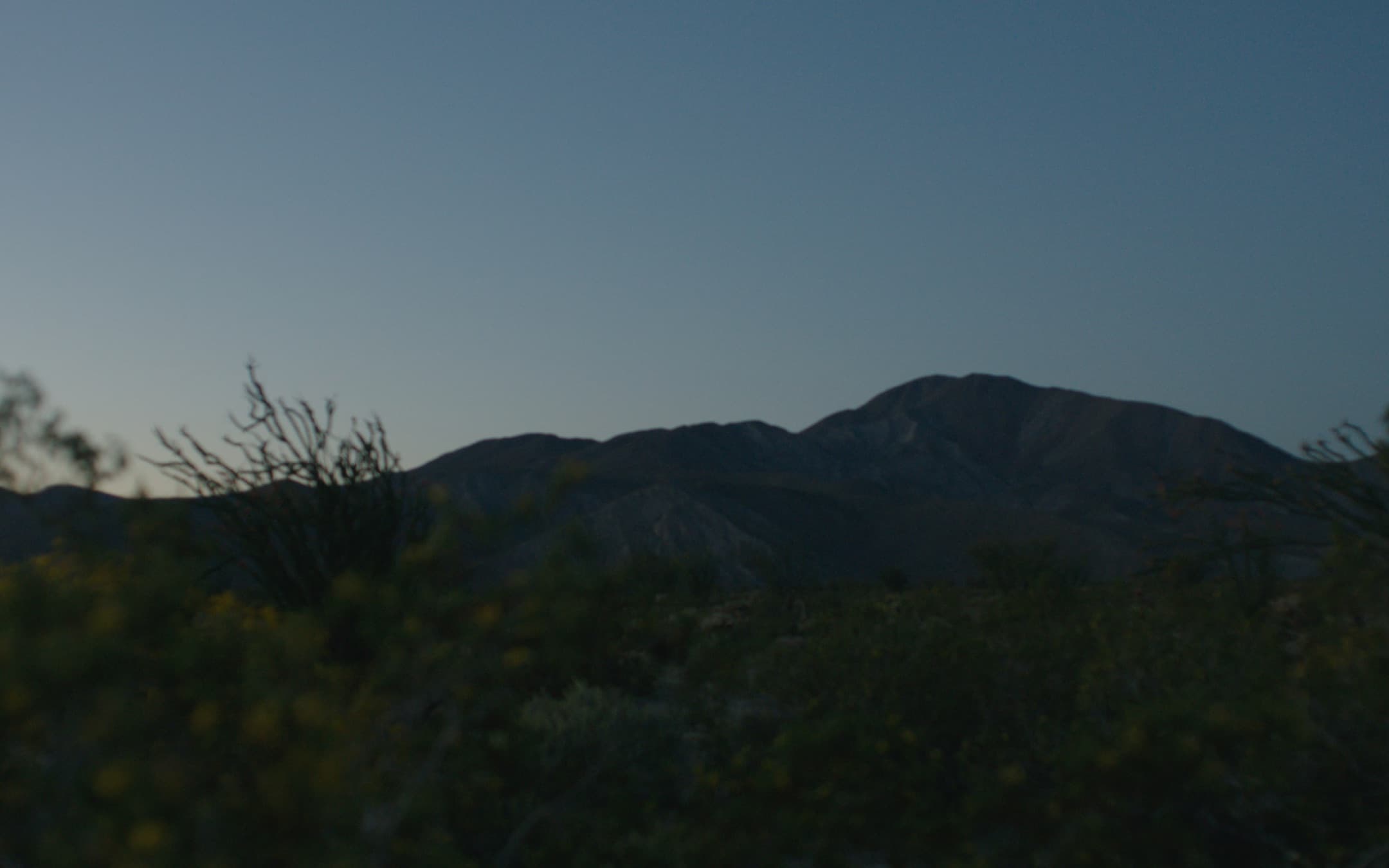 Desert sunrise with a dark mountain ridge under a deep blue sky