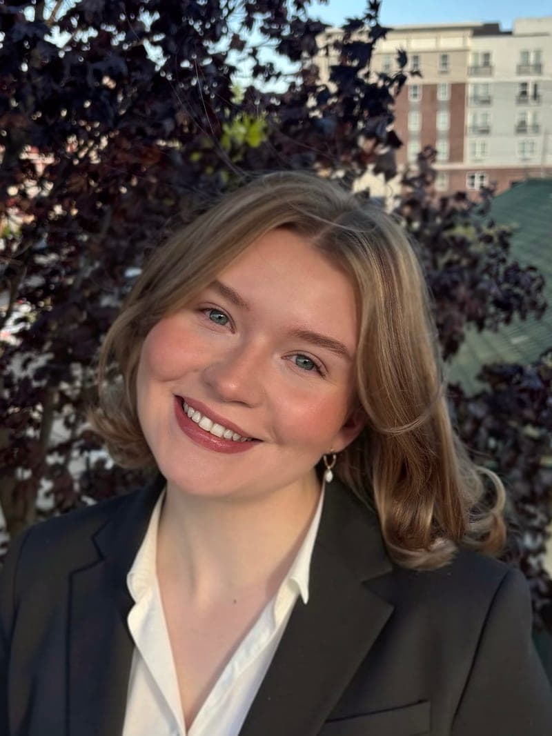Anelle Mouton smiling outdoors in front of a purple-leaf tree