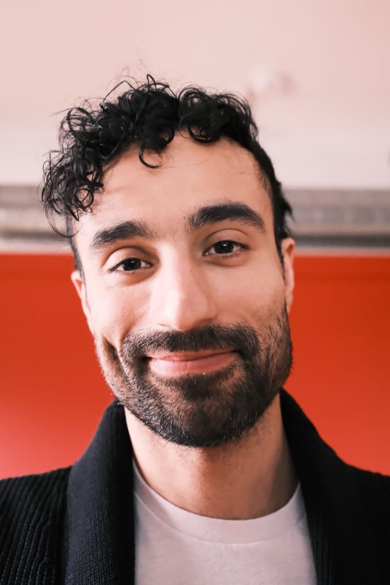 Georgios Katsikis smiling in front of a red wall